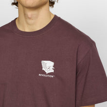 Load image into Gallery viewer, A close-up of a man wearing a dark plum-brown crewneck t-shirt with a small white graphic and the word 'REVOLUTION' printed on the left chest, against a light gray background.